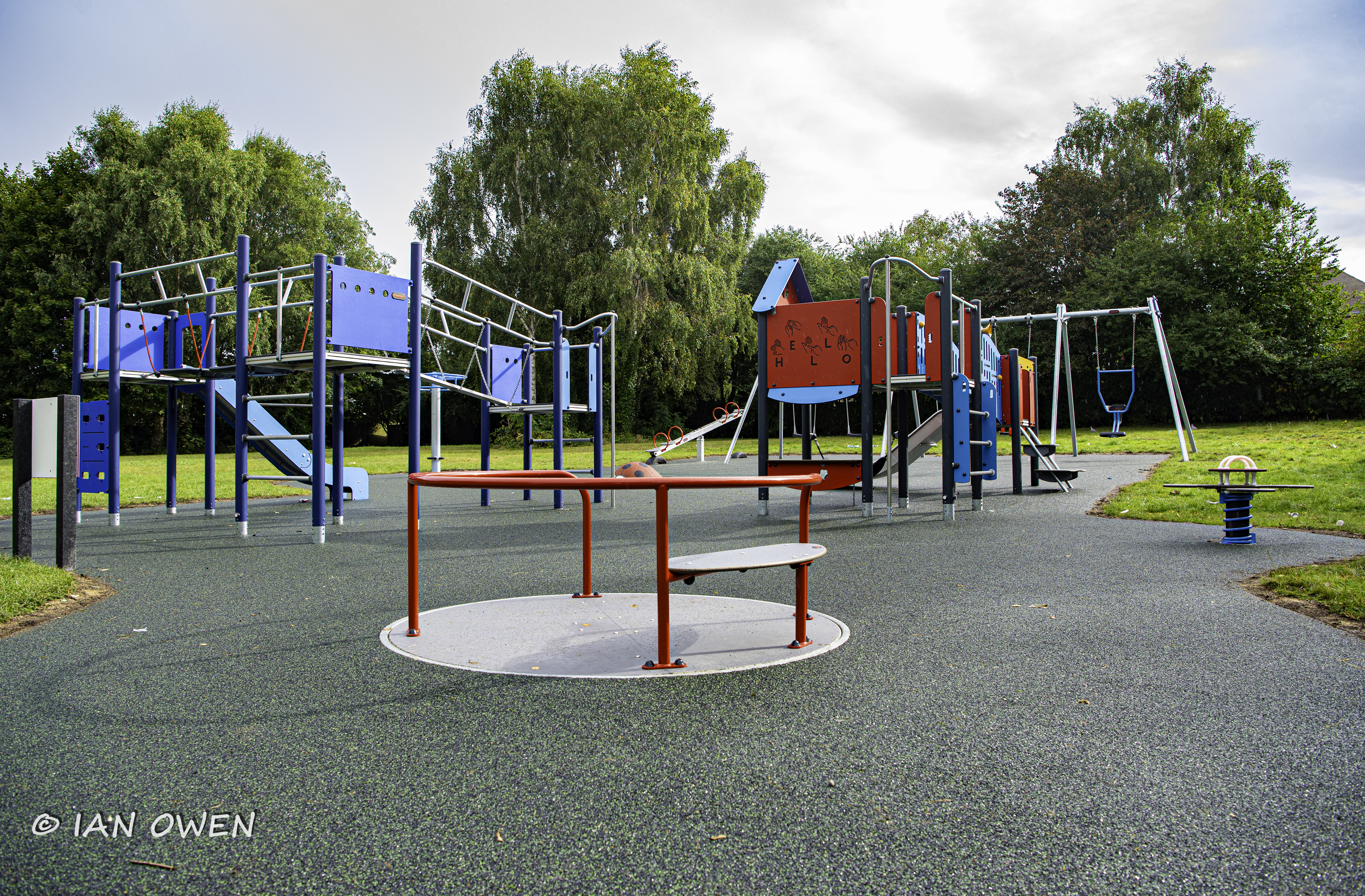 photo of playground equipment, including a blue climbing frame with a slide and a red climbing frame and swings