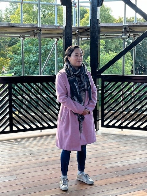 Cllr Nova Arkney standing inside the refurbished bandstand wearing a pink coat and scarf