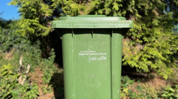 a green waste garden bin in front of a green bush